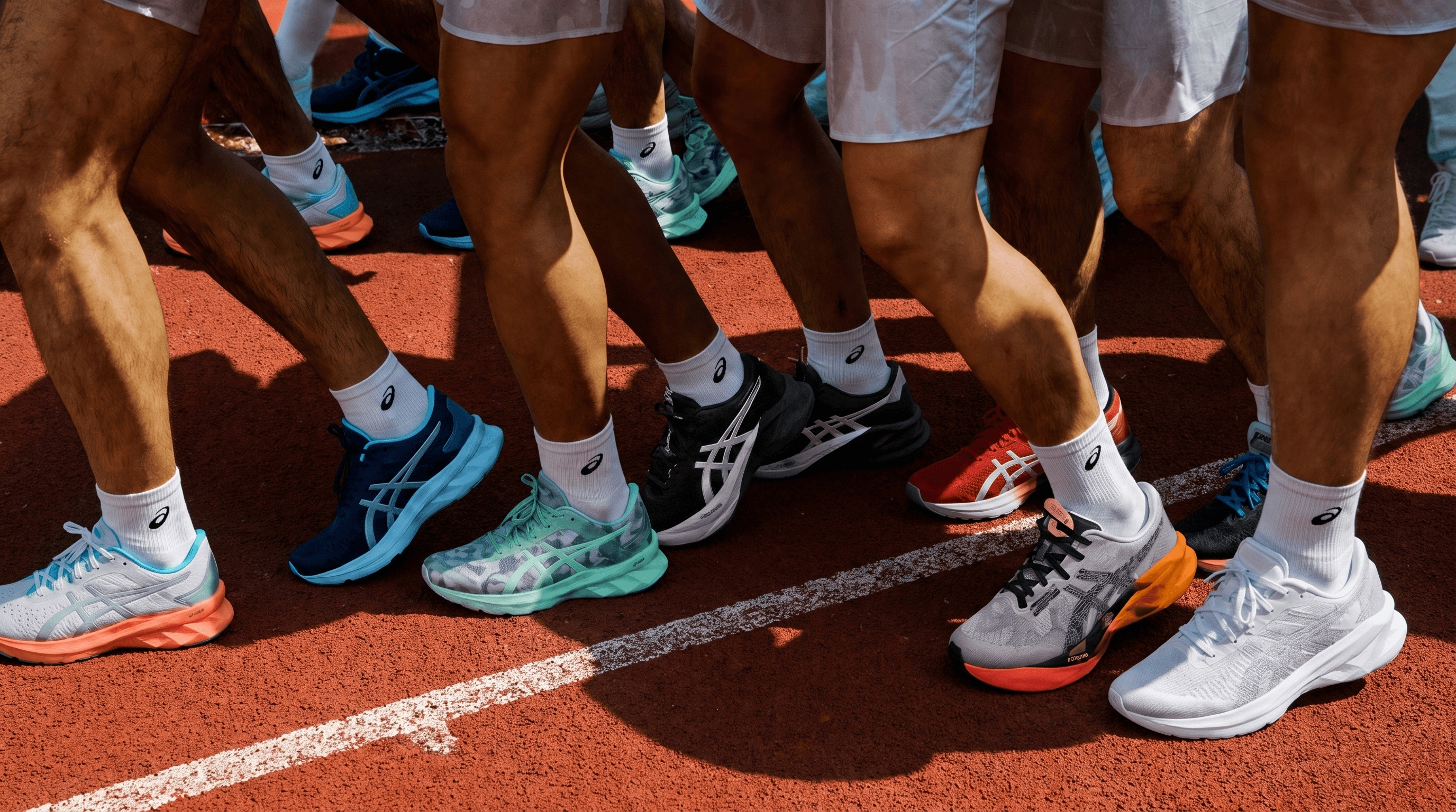Runners' legs mid-stride in a row of Asics trainers on a red running track, shot low and close to the ground