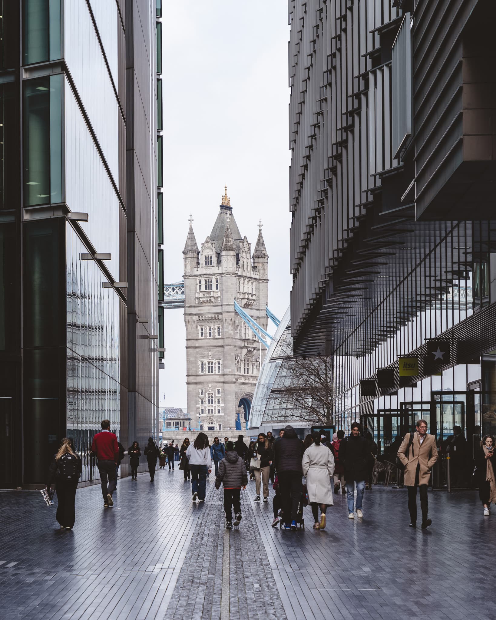 Tower Bridge at the end of a wet Bermondsey street, commuters walking towards it.