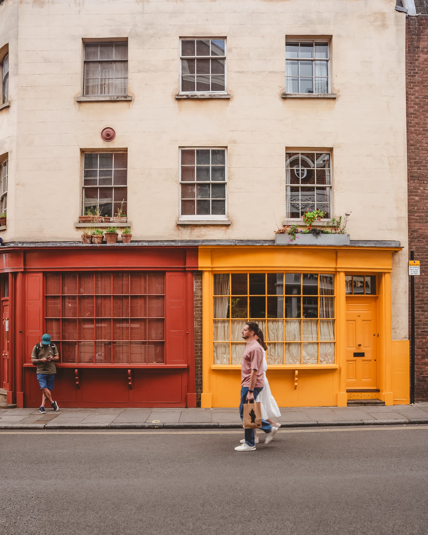 A terrace of orange and red shopfronts, a passer-by crossing the frame.