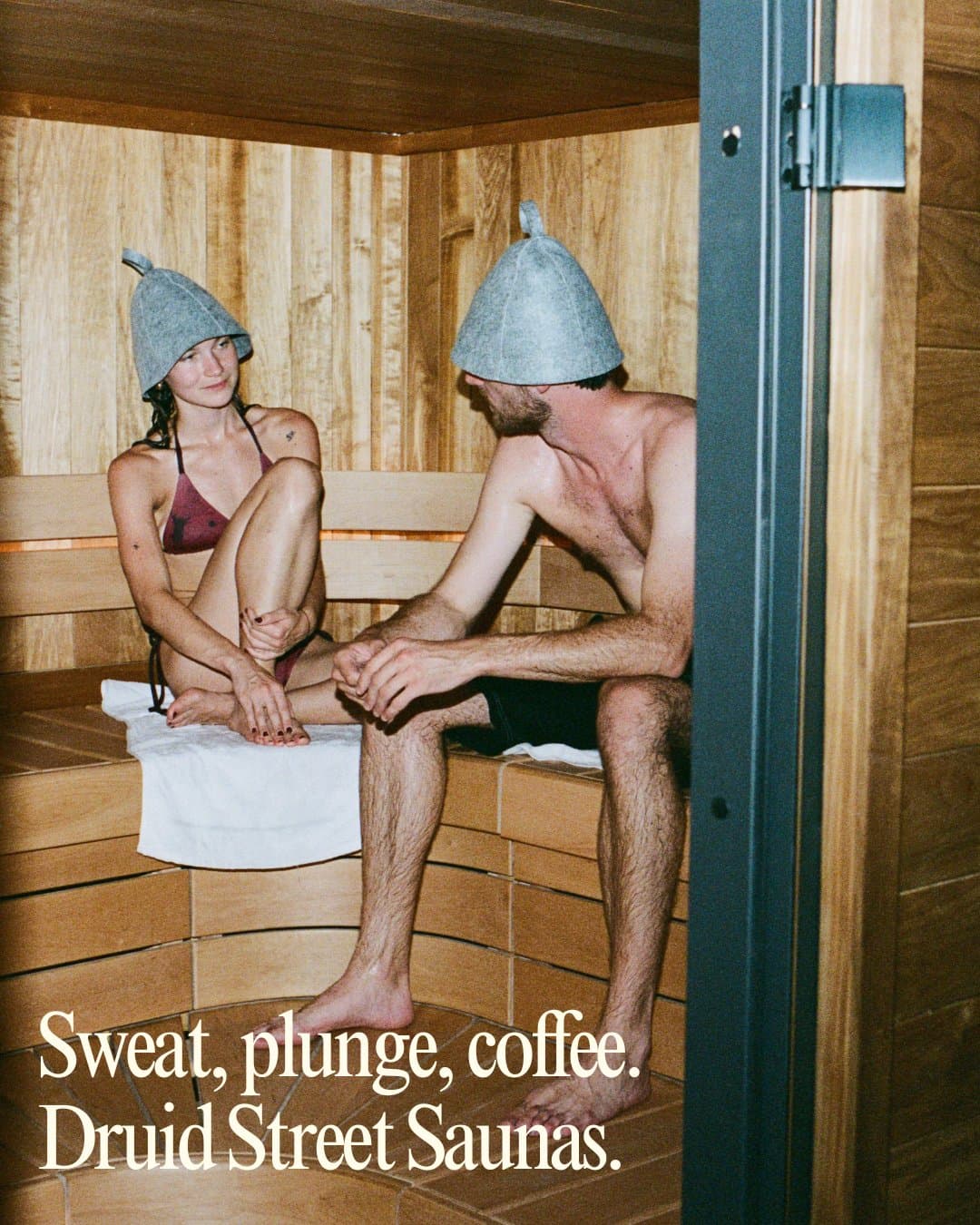 Two people sitting in a sauna in felt hats, from a Druid Street Saunas post.