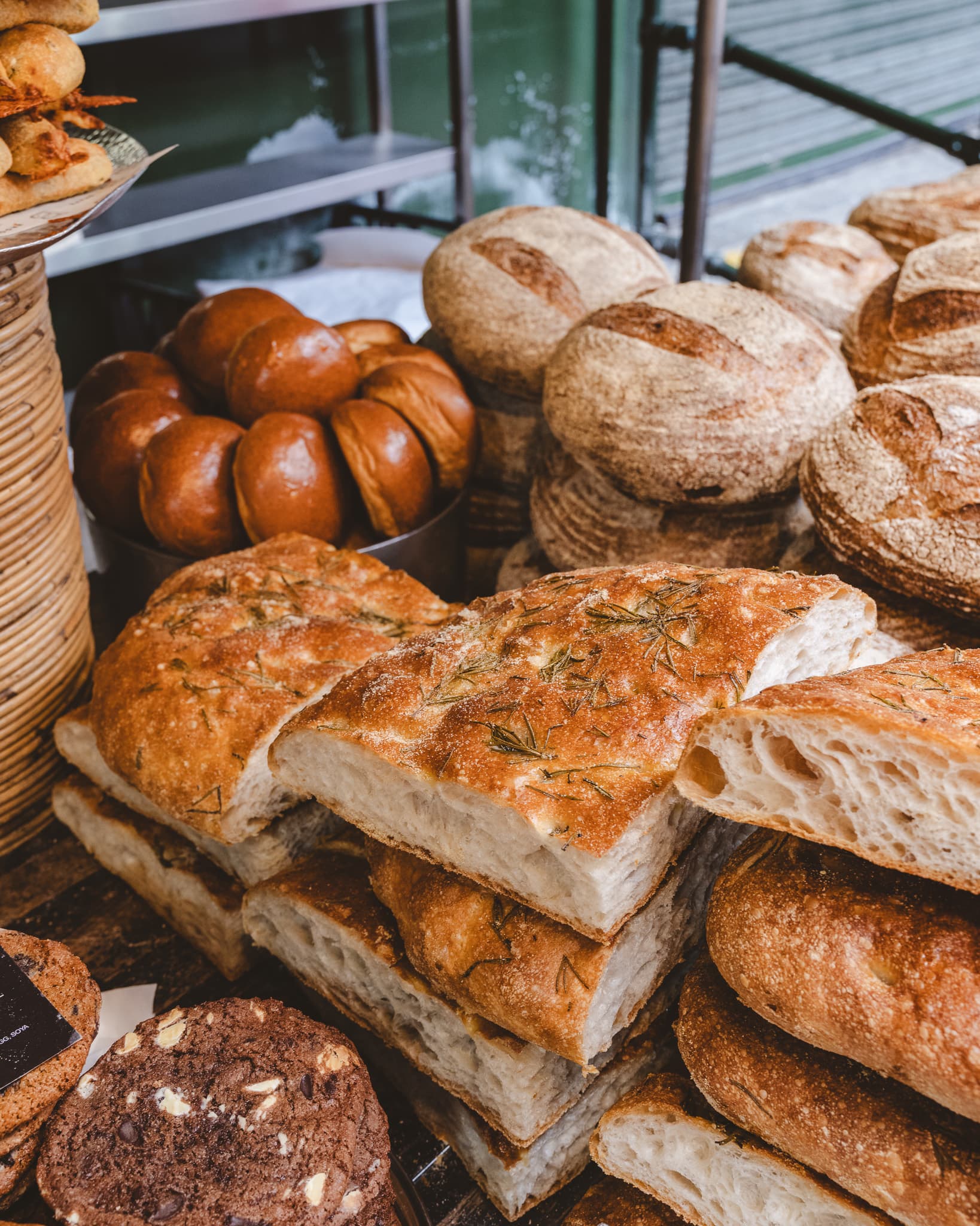 A bakery counter stacked with sourdough loaves, bread rolls and rosemary focaccia.