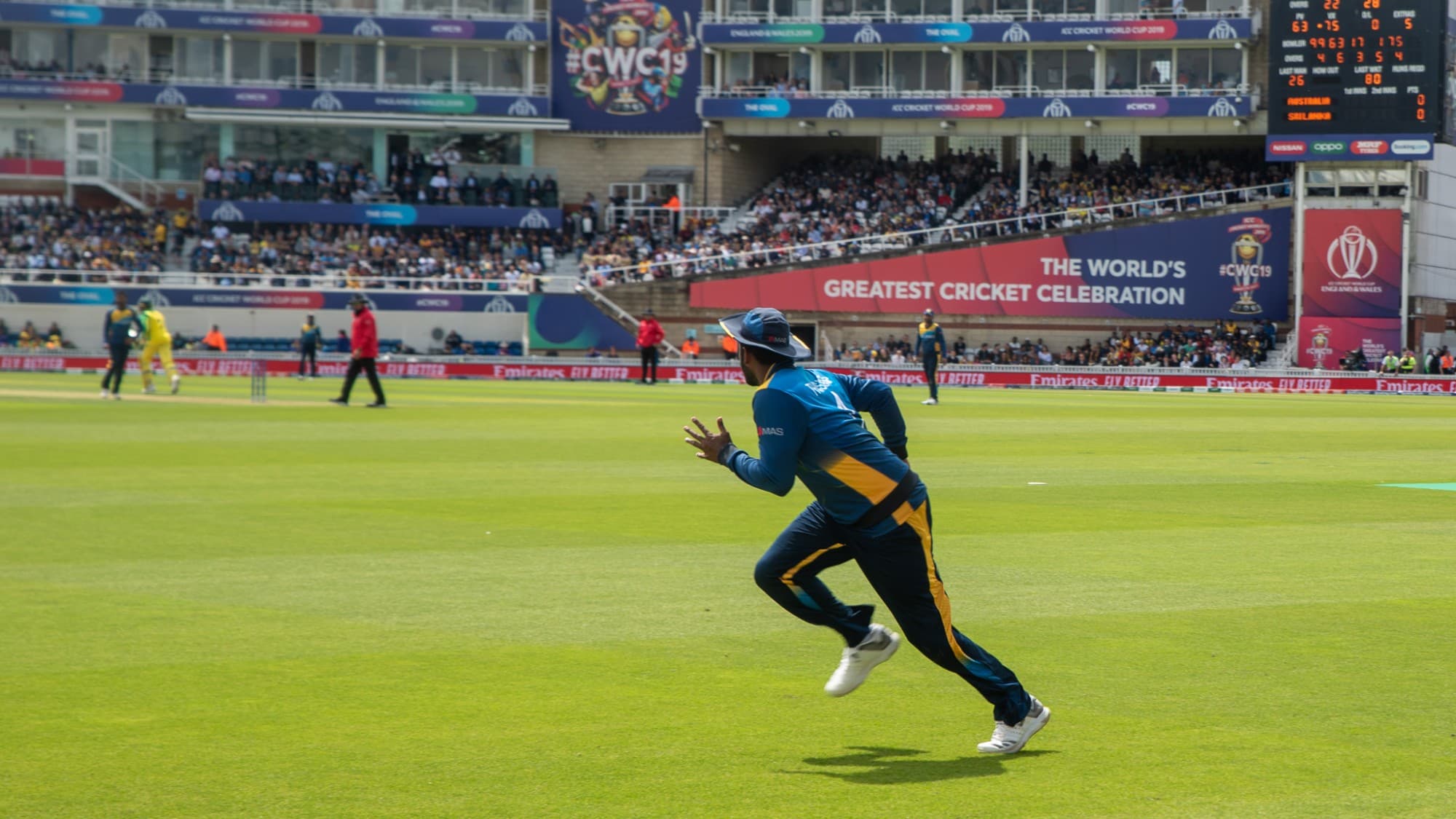 A fielder sprints across the outfield, a big screen reading the world's greatest cricket celebration behind him.